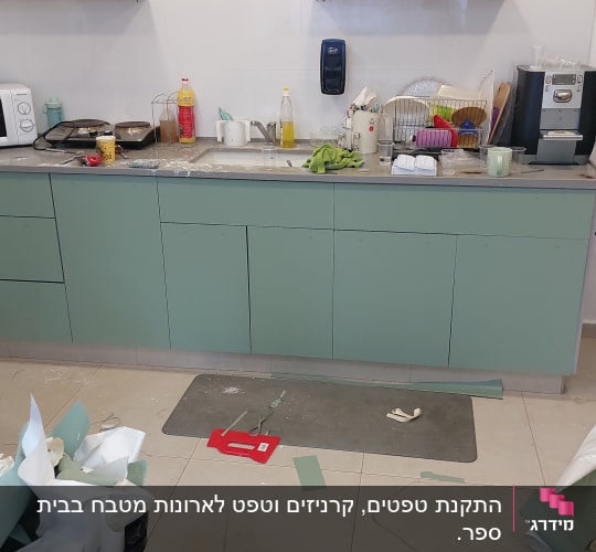מטבח עם ארונות ירוקים, כלים בכיור וניירות על הרצפה